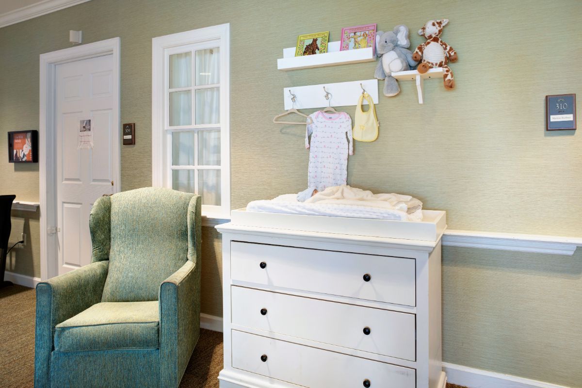 A cozy nursery with a white changing table and a green armchair.
