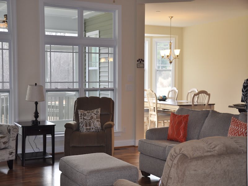 A cozy living room with an armchair, sofa, and a dining area in the background, filled with natural light.
