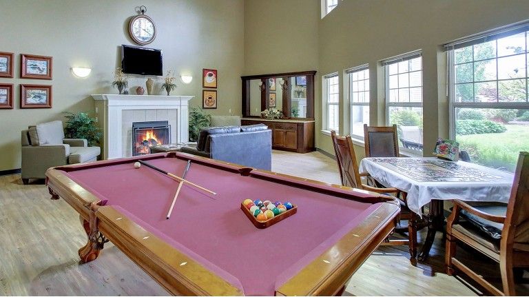 A cozy living room featuring a pool table, fireplace, and large windows.