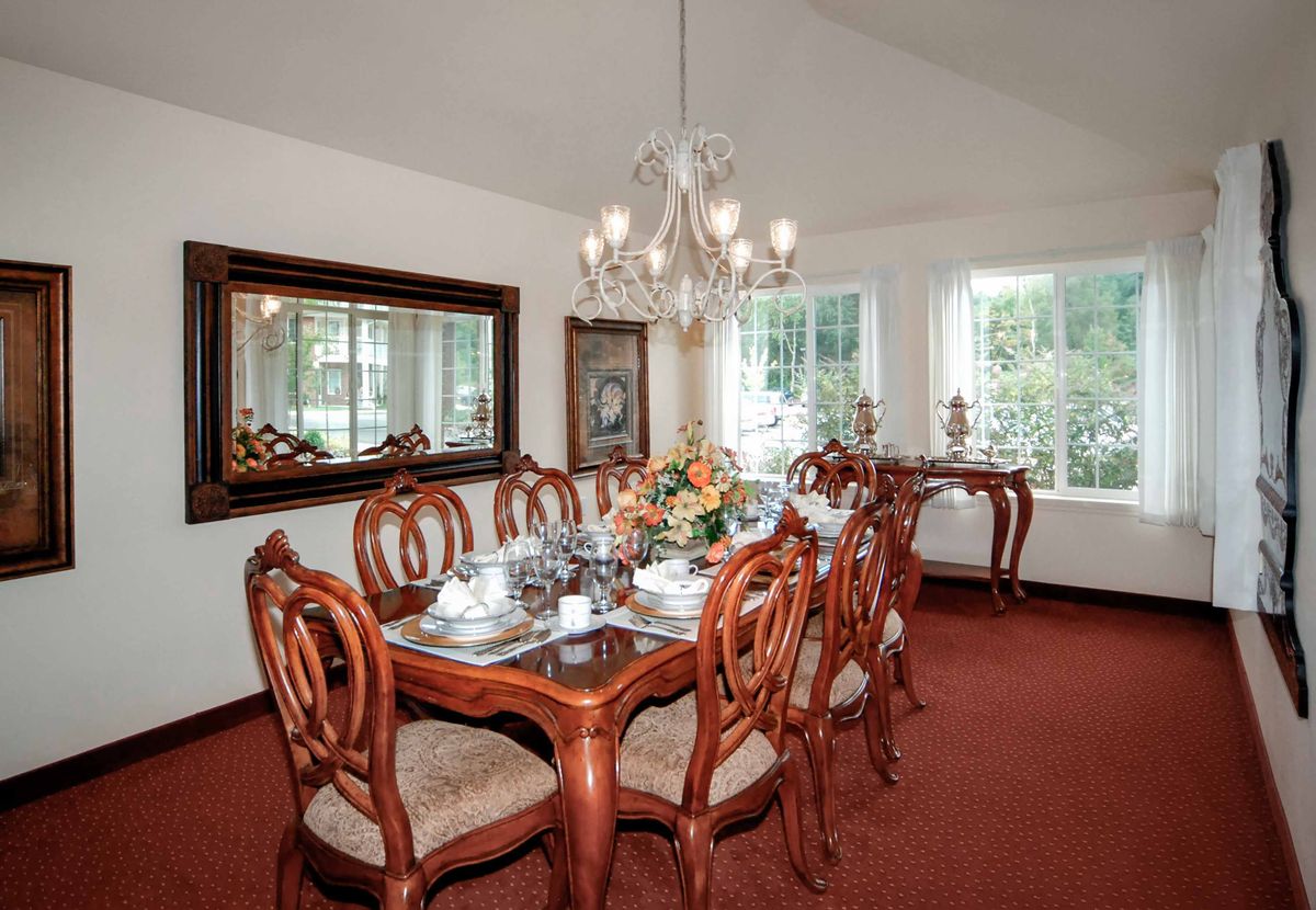 A beautifully designed dining room featuring a wooden table set with elegant chairs, complemented by a chandelier and large windows.