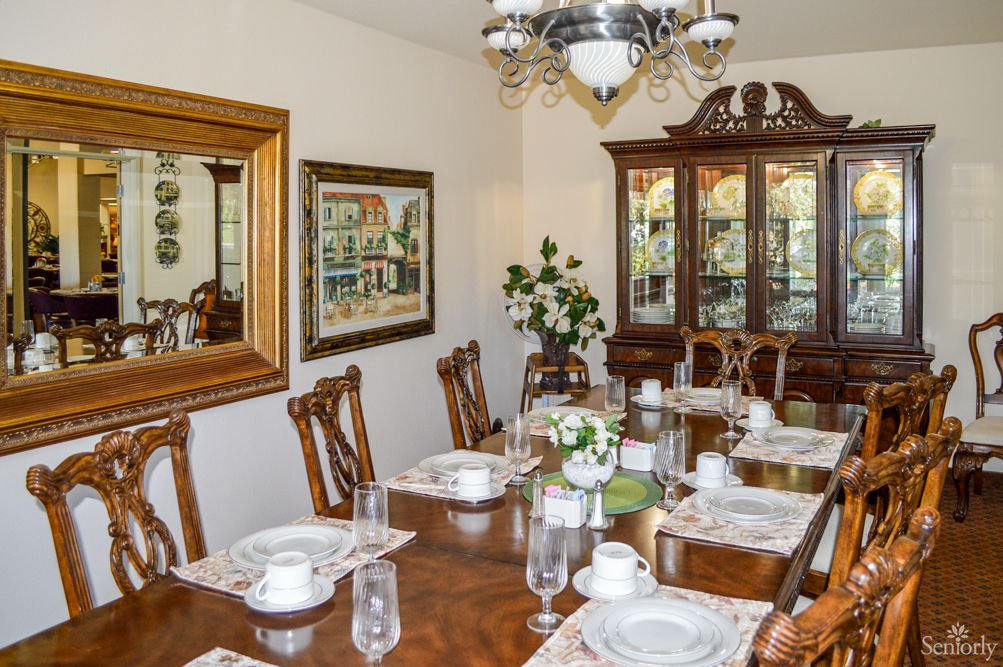 A formal dining room with a long wooden table, elegantly set for a meal, featuring a chandelier and a china cabinet.