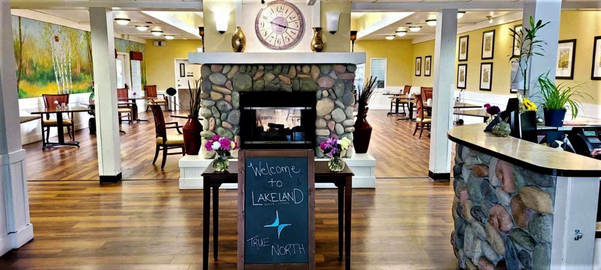 A welcoming lobby with a rustic stone fireplace, a clock above it, and decorative flowers on either side of a greeting sign.