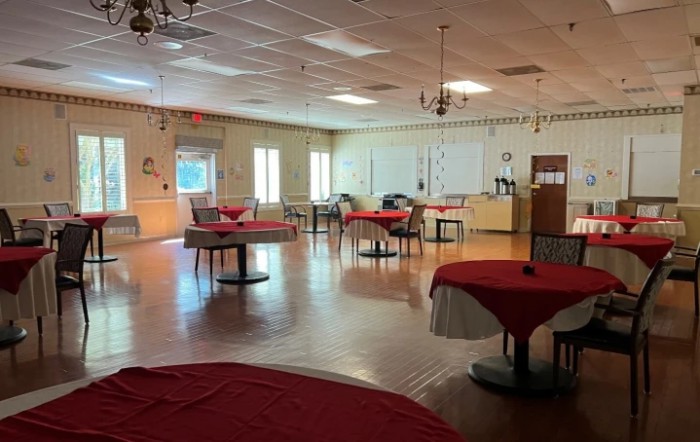 An empty event space with tables covered in red tablecloths and chairs arranged around them.