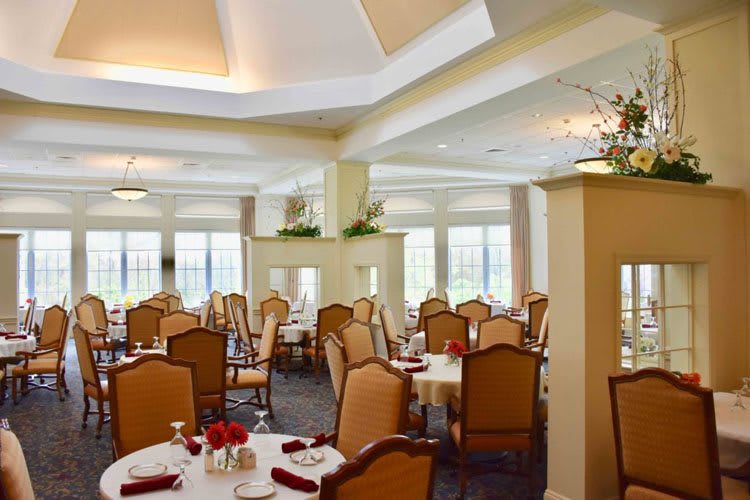 An elegantly decorated dining room with neatly arranged tables and chairs, featuring soft lighting and floral accents.