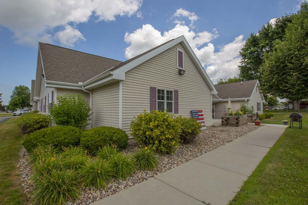 A suburban house with a well-maintained garden and a concrete pathway under a partly cloudy sky.