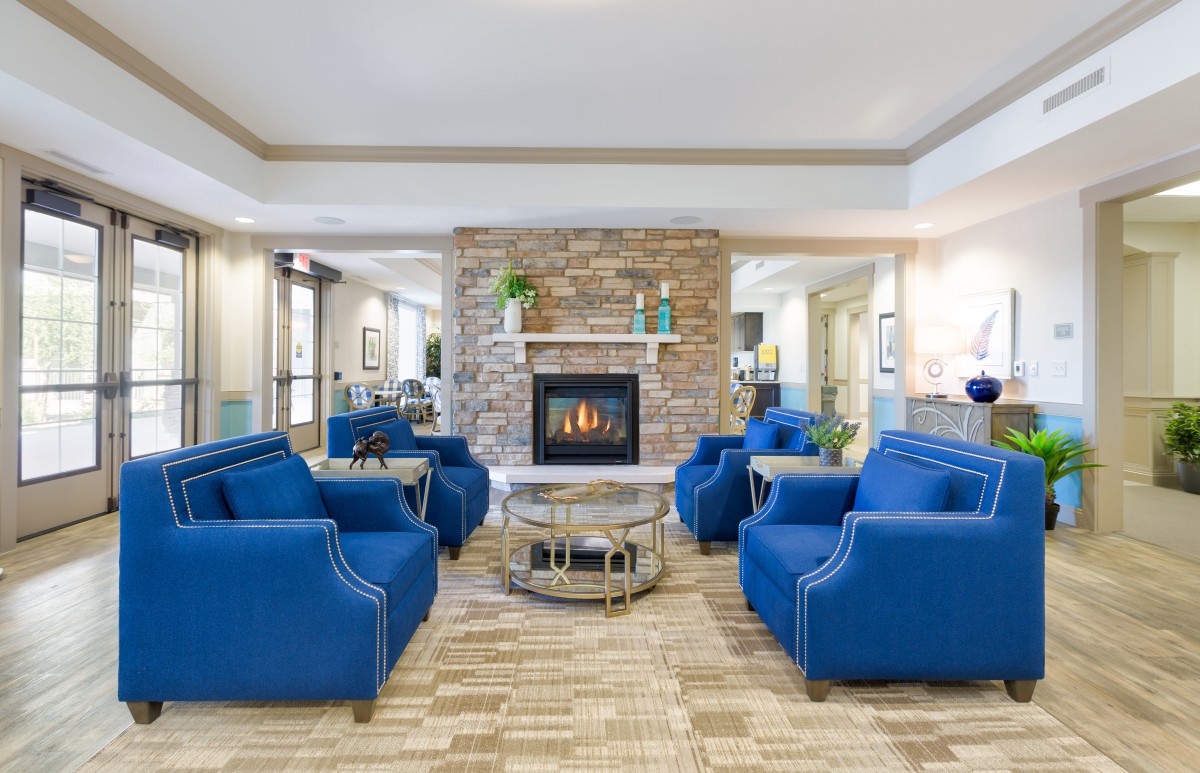 A modern living room with a central fireplace, surrounded by blue chairs creating a cozy seating area.