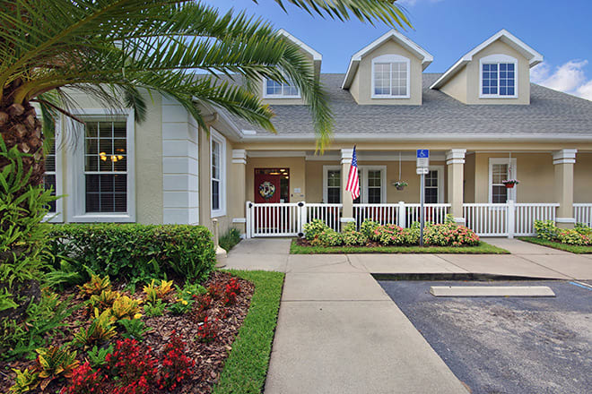A charming suburban house with a welcoming porch, surrounded by manicured landscaping and displaying an American flag.