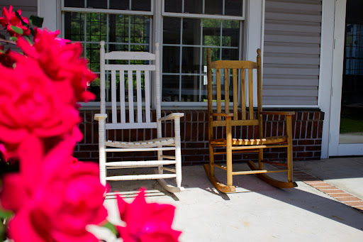 Two rocking chairs sit invitingly on a sunny porch, surrounded by vibrant flowers.