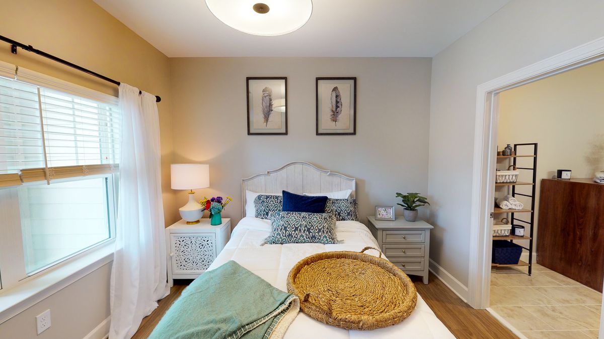 A cozy bedroom interior with a neatly made bed, decorative pillows, and artwork on the walls.