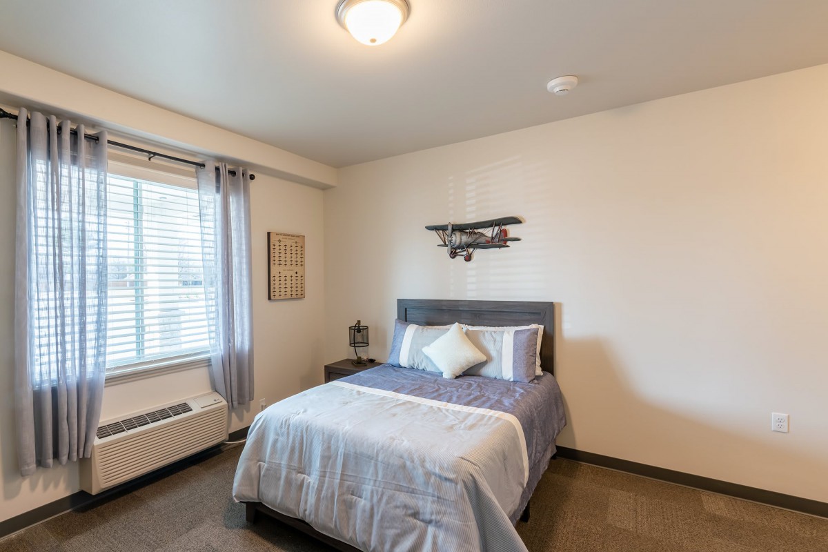 A modern bedroom with a neatly made bed, window with curtains, and simple decor.