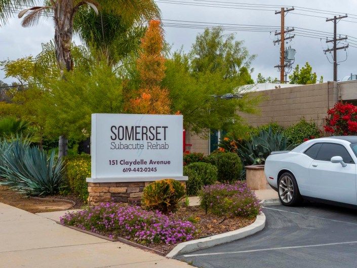 Entrance sign for Somerset apartment homes surrounded by landscaping and adjacent to a parked car.