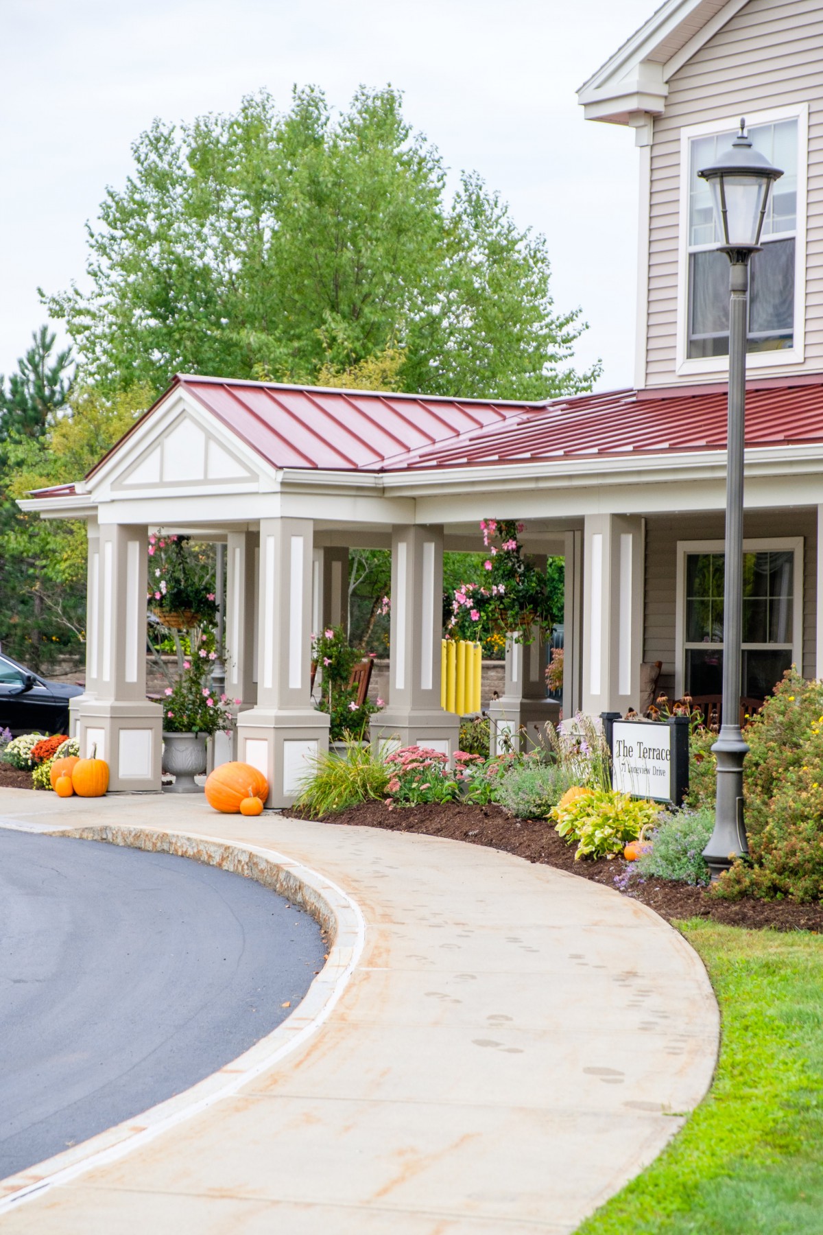 A charming house with a red roof, adorned with pumpkins and seasonal decorations, surrounded by landscaped gardens.