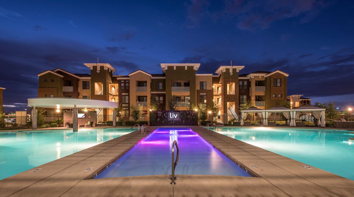 A luxurious apartment complex illuminated at night, featuring a central swimming pool with colorful lighting.