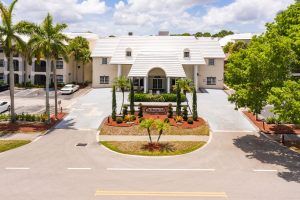 A large residential house with a driveway and palm trees on a sunny day.