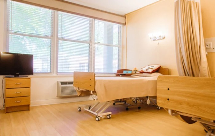 A clean and well-lit hospital patient room with a single bed and large windows.
