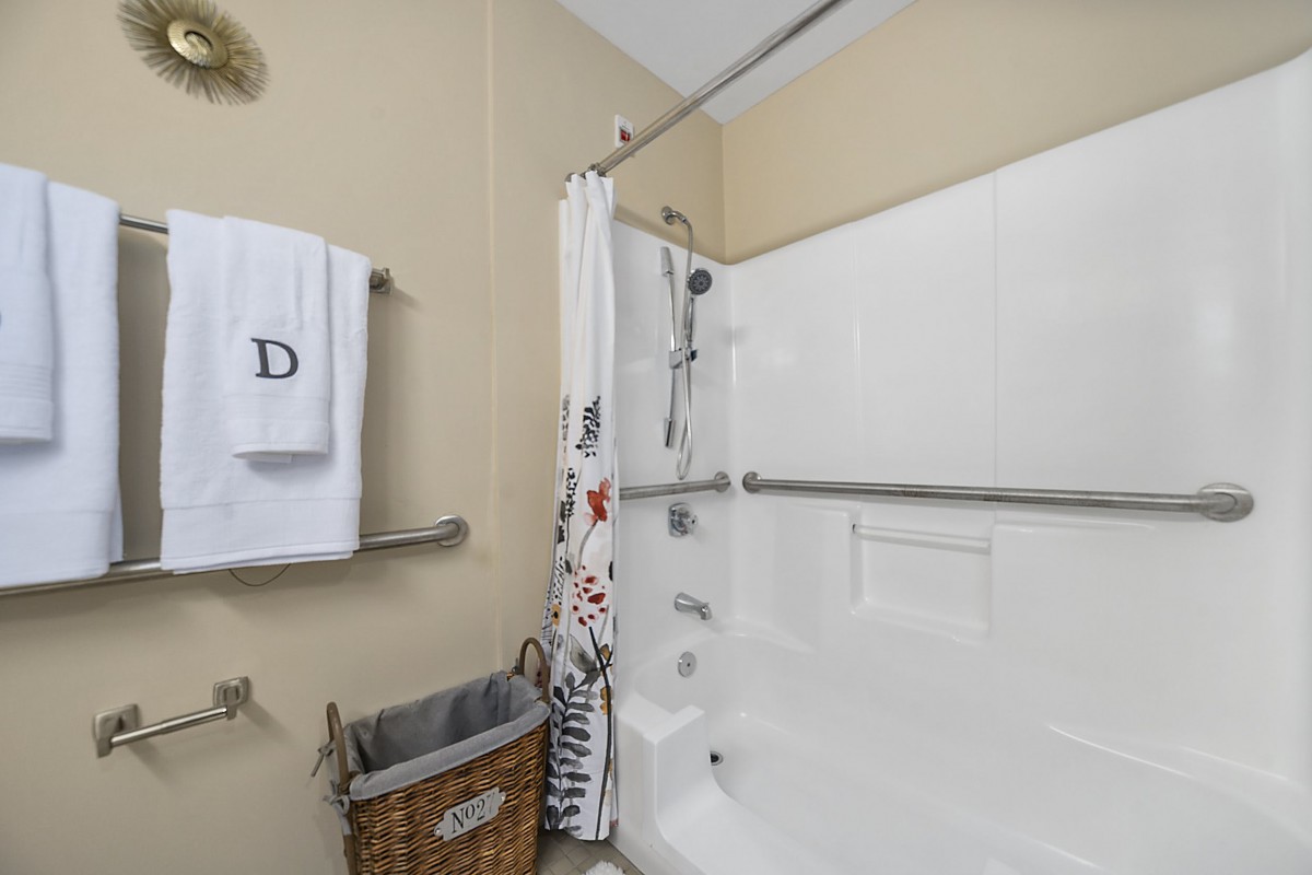 A bathroom featuring a shower with a curtain, grab bars, and neatly hung towels beside a woven basket.