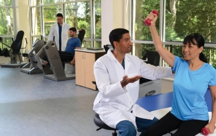 A healthcare professional assists a patient with physical therapy exercises in a clinic setting.