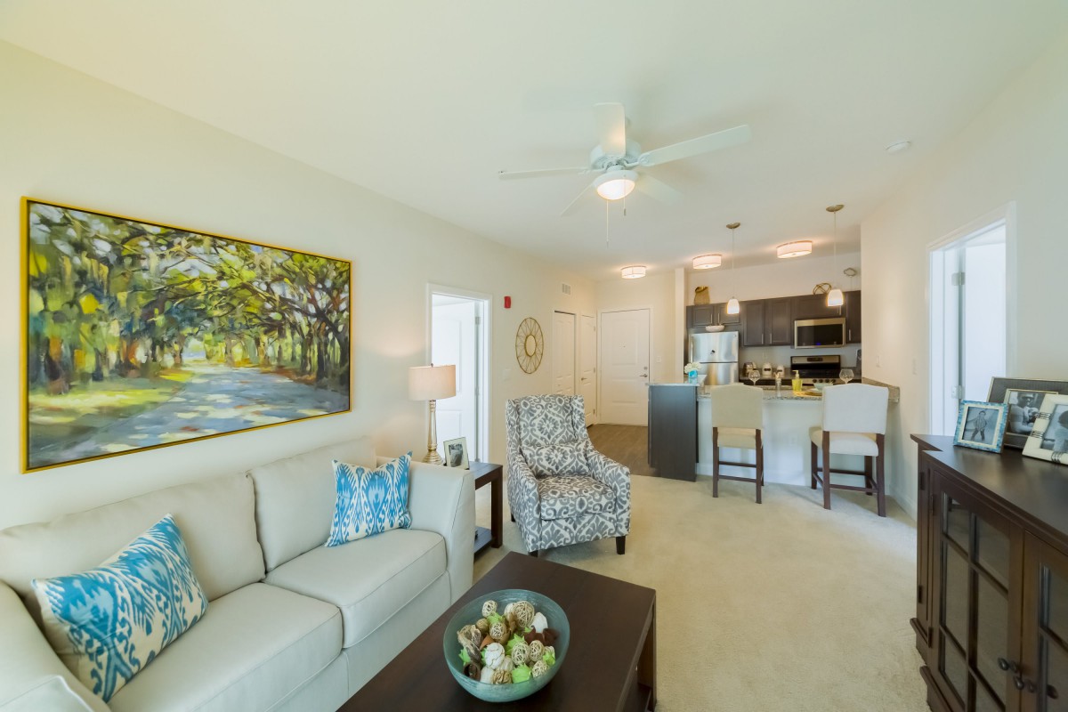A spacious open-plan living room with modern furnishings and a view into the kitchen area.