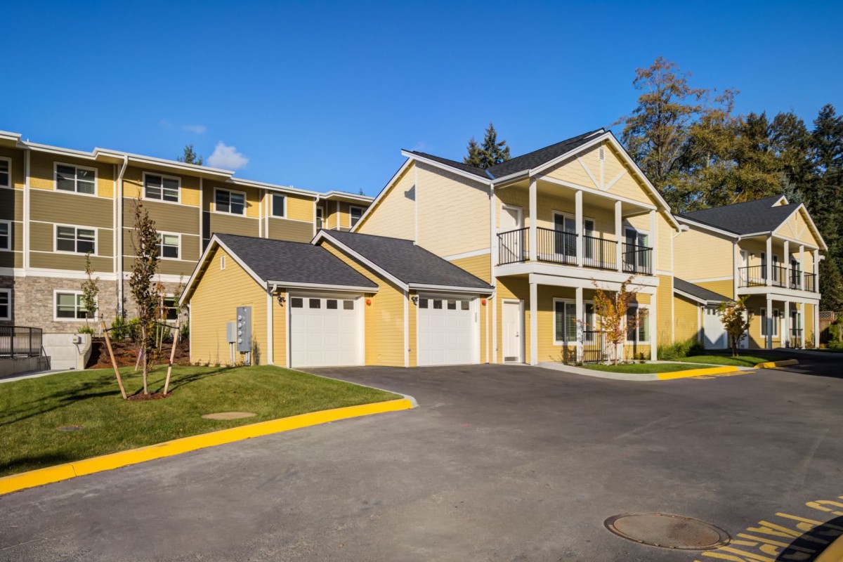 A two-story yellow house with garages under a clear blue sky.