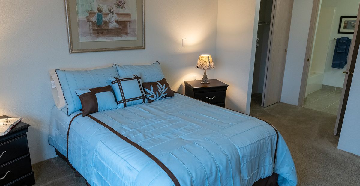 A cozy bedroom with a neatly made bed and a lamp on the nightstand.