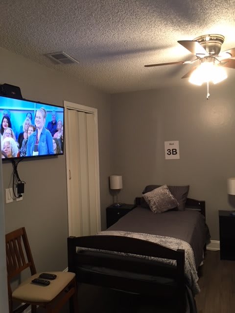 A modern bedroom with a single bed, wall-mounted TV, and ceiling fan.