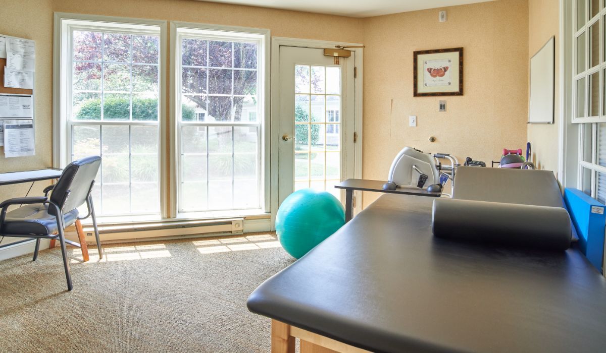 A well-lit exercise room featuring a yoga ball, massage table, and therapy equipment.