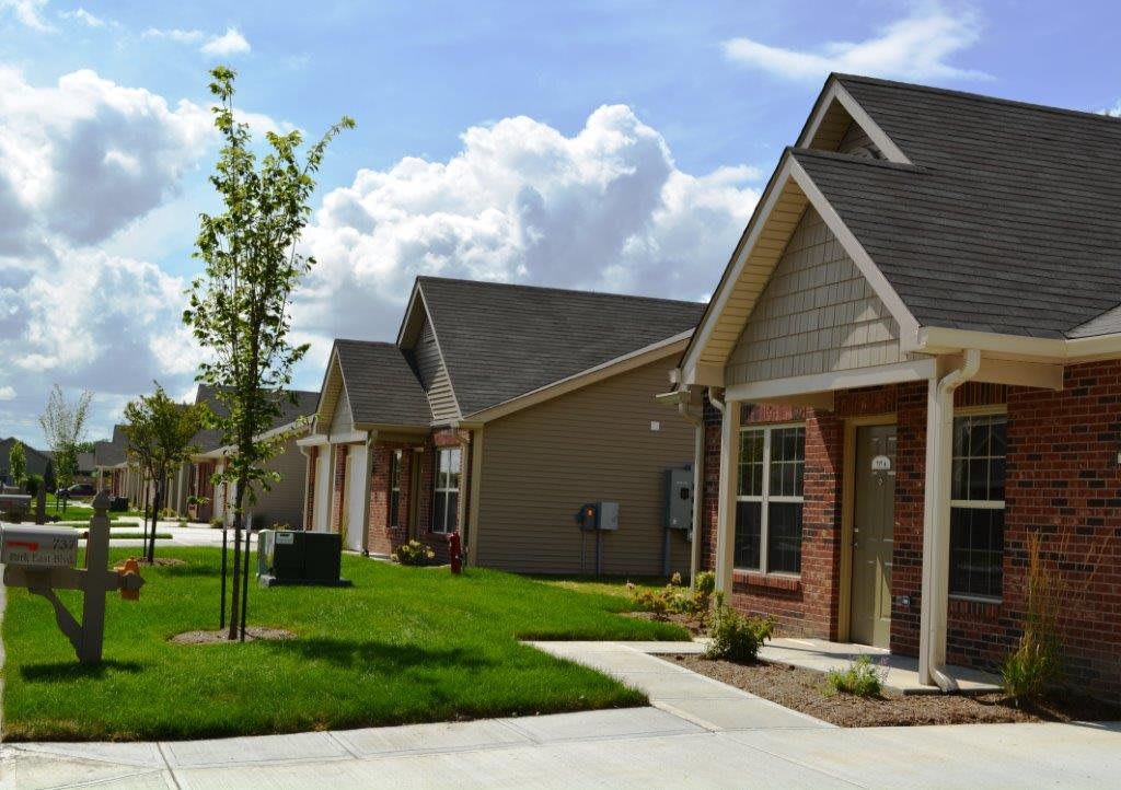 A row of suburban houses with neatly maintained lawns and driveways on a sunny day.