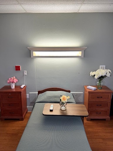 A serene hospital room featuring a single bed, nightstands with flowers, and modern lighting.