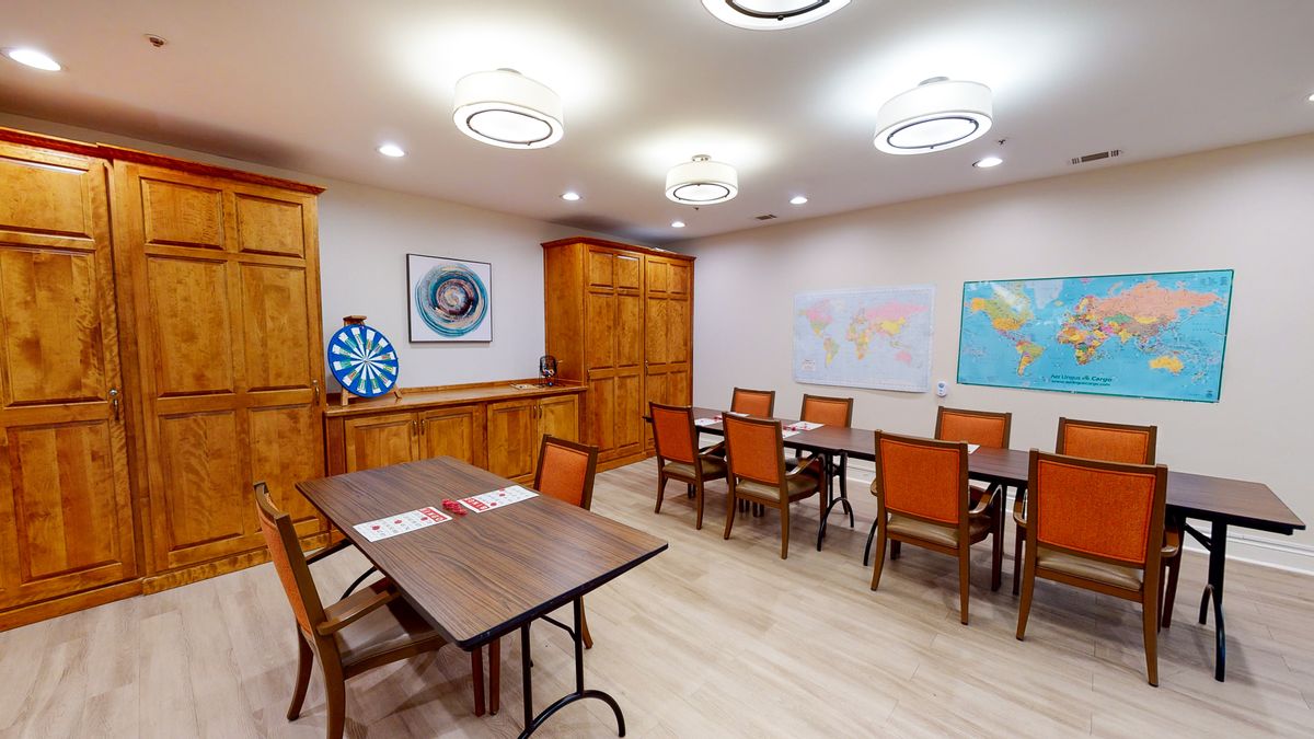 A well-lit conference room with tables, chairs, a dartboard, and world maps on the walls.