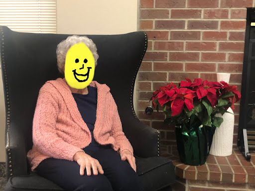 A cheerful elderly woman sitting comfortably in a chair, surrounded by festive potted plants.