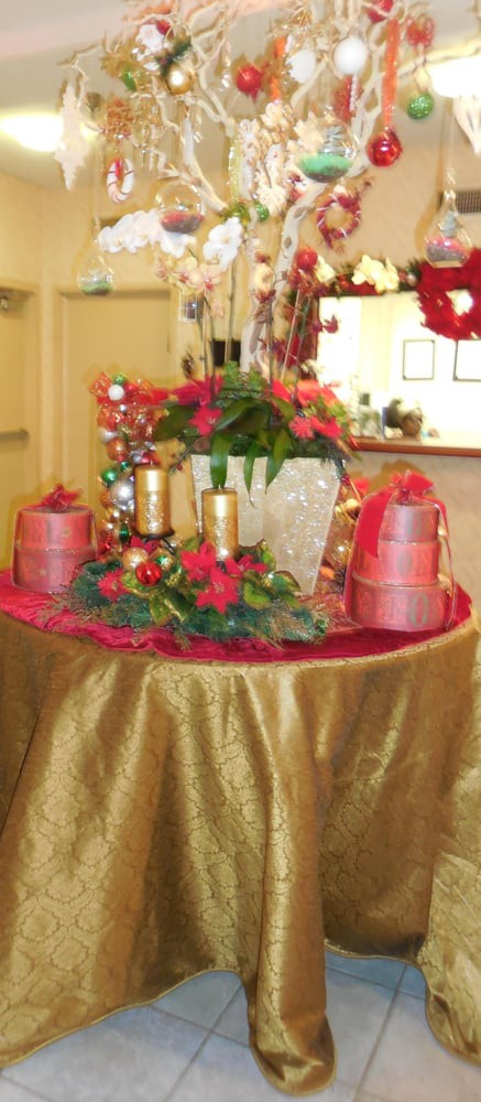 A festive table centerpiece featuring candles, flowers, and decorative ribbons in a red and gold color scheme.