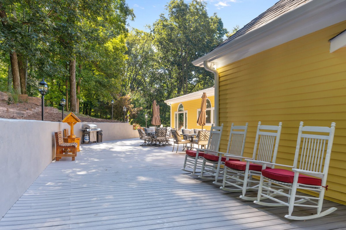 A sunny deck with rocking chairs and patio furniture outside a yellow house.