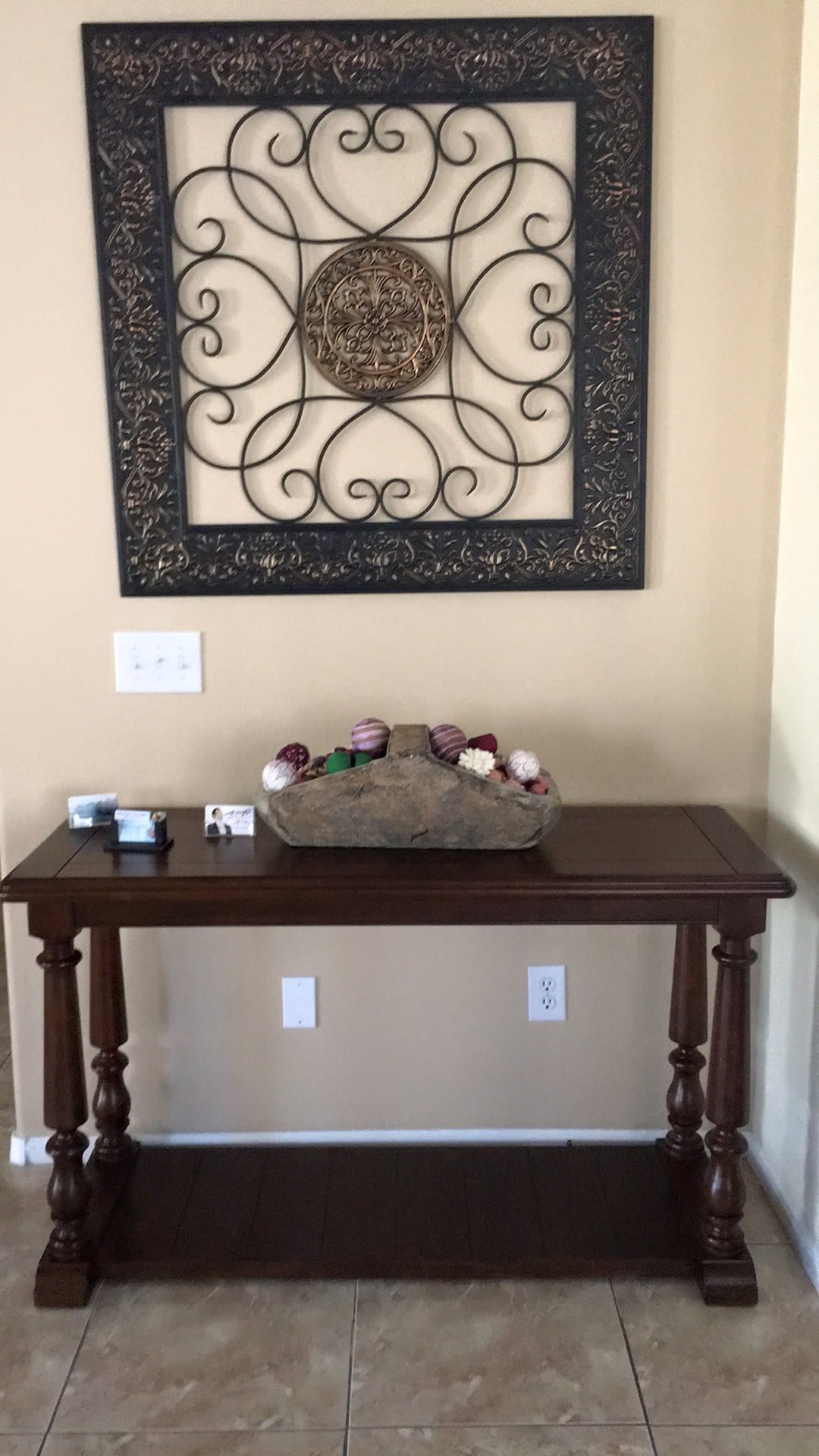 A wooden console table with floral decorations below an ornate wall art piece.