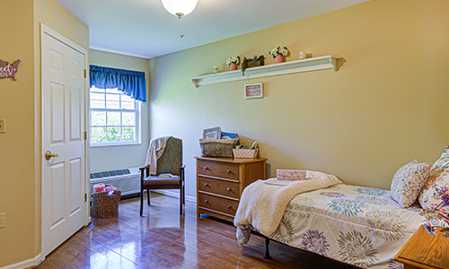 A cozy bedroom featuring a single bed, dresser, and a window with blue curtains.