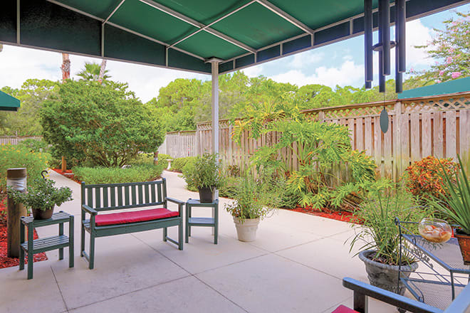 A cozy patio with benches and potted plants under a green awning.