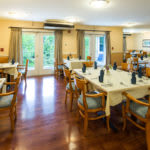A cozy dining room with neatly arranged tables and chairs, featuring a warm interior design and wooden flooring.