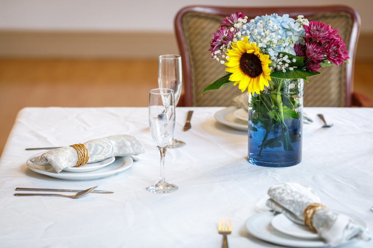 A beautifully set dining table with a vase of colorful flowers and elegant place settings.
