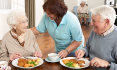 A caregiver assists elderly individuals during a meal at a nursing home.