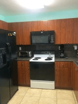 A kitchen with wooden cabinets, a black refrigerator, oven, microwave, and countertop appliances.