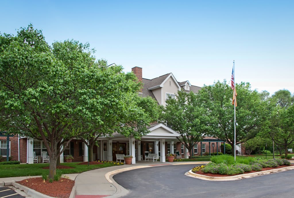 A well-maintained building entrance surrounded by trees with a flagpole and circular driveway.