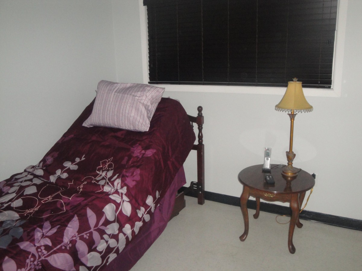 A small bedroom with a single bed, lamp, and nightstand next to a window.