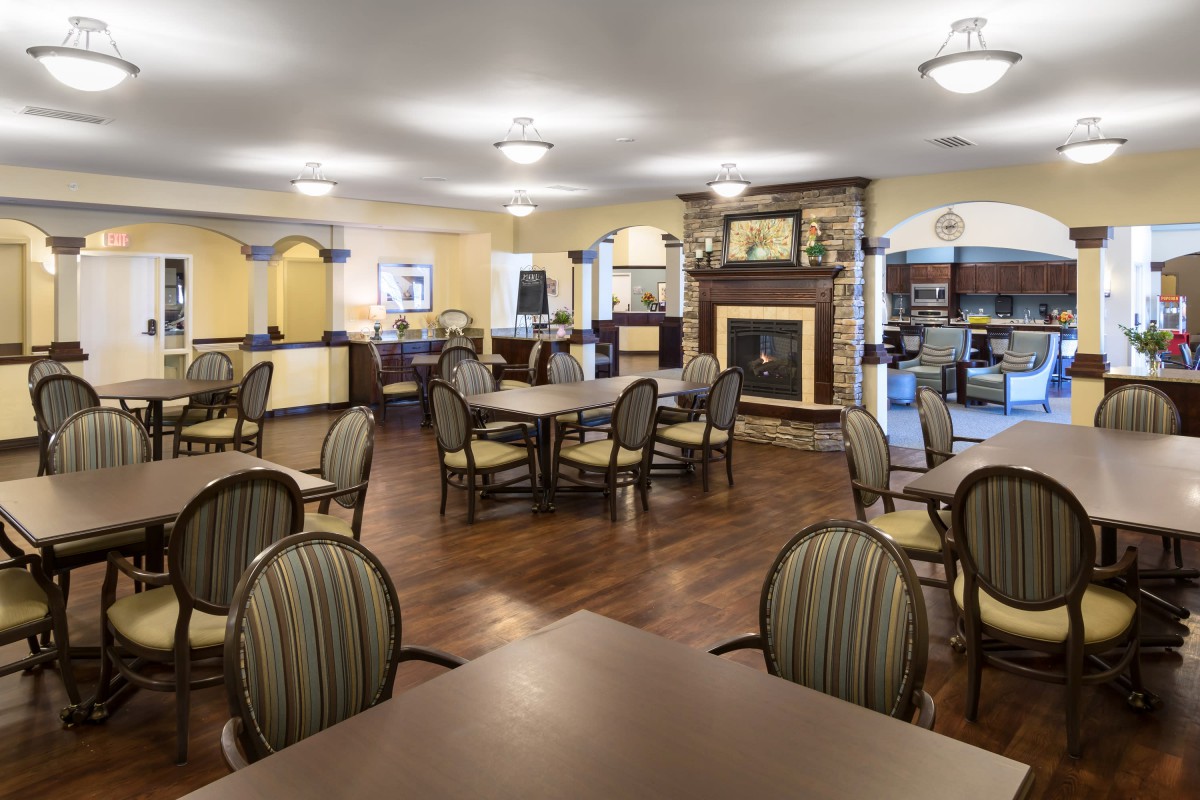 A spacious dining room with wooden floors, arranged tables and chairs, and a fireplace.