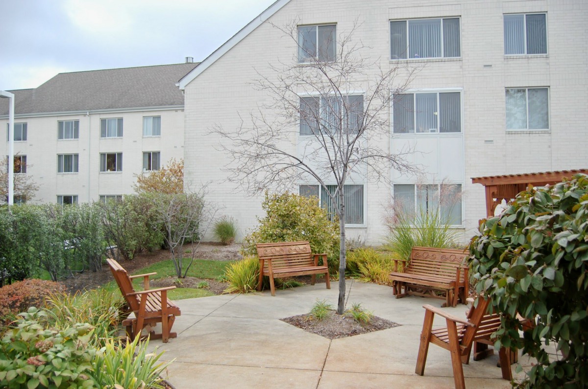 A serene courtyard with wooden benches and lush landscaping outside a residential building.