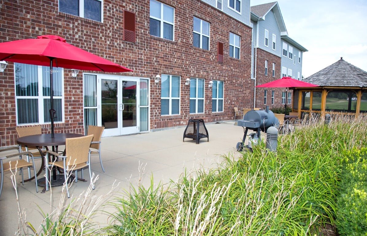 A patio area with outdoor seating and red umbrellas in front of a brick building.