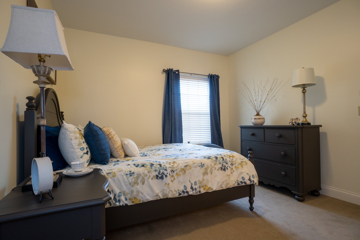 A cozy bedroom with a neatly made bed, dark furniture, and a window with curtains.