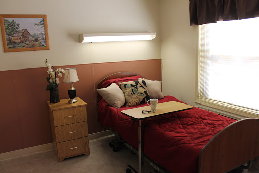 A cozy bedroom featuring a bed with red bedding, a nightstand with a lamp, and a small table tray.