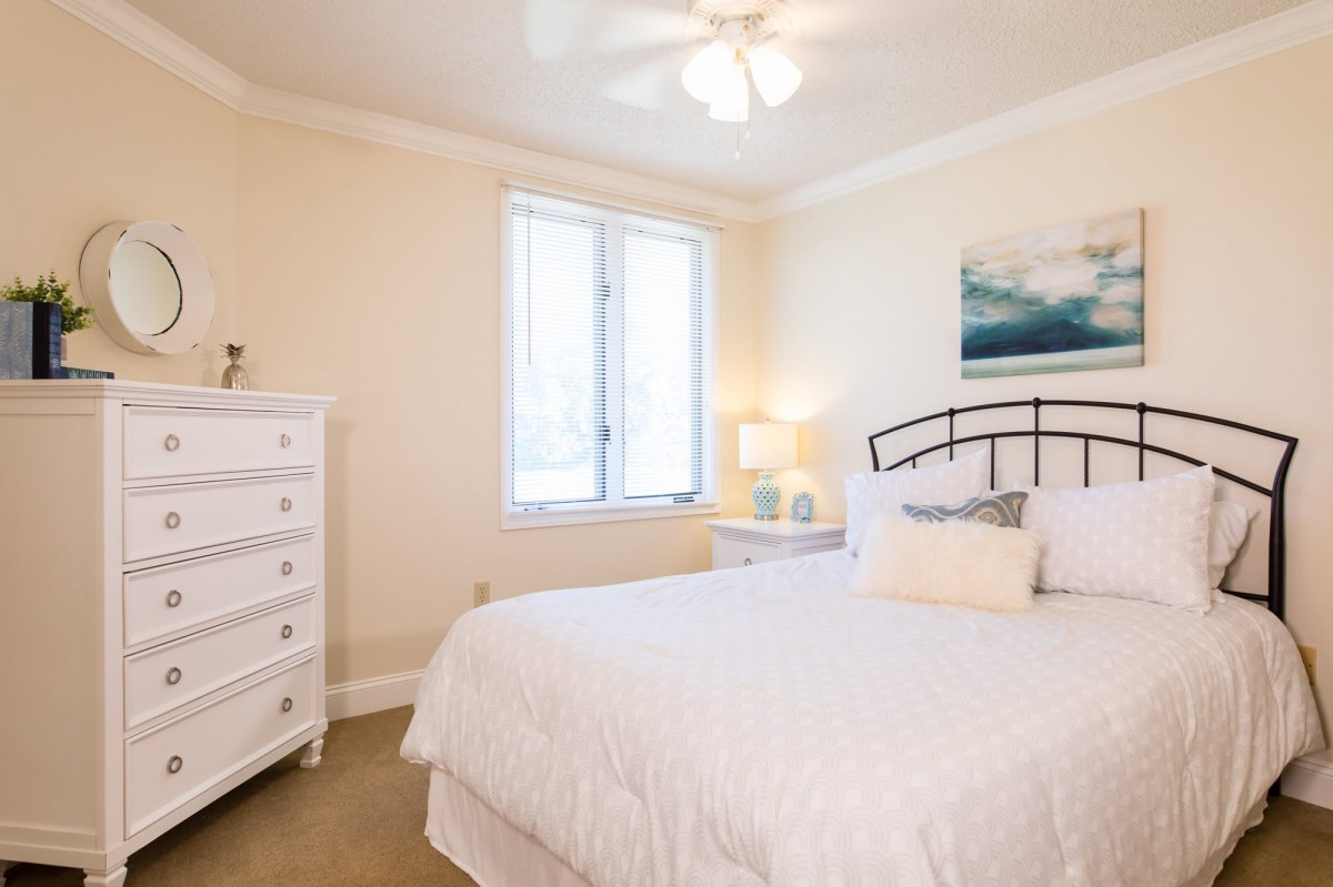 A cozy bedroom with a neatly made bed, white walls, and simple decor.