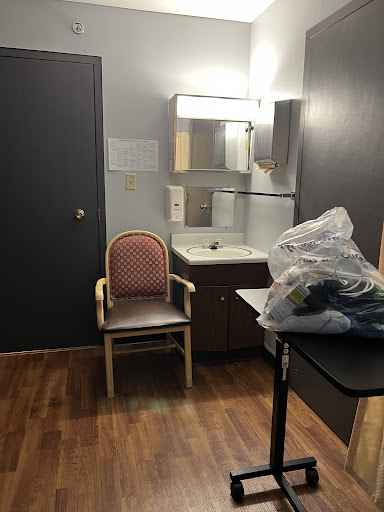 A simple interior of a room featuring a chair, mirror, and a table with some items.