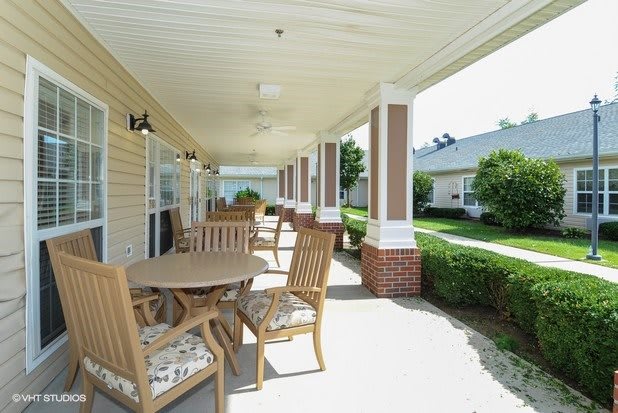 A sunny porch with wooden chairs and tables overlooking a garden.