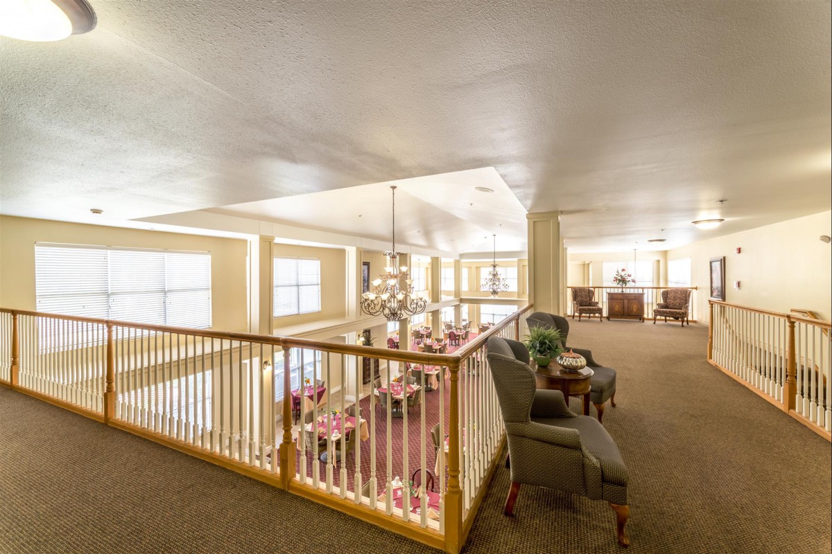 A spacious living area with comfortable seating and large windows, featuring a chandelier and wooden banister.